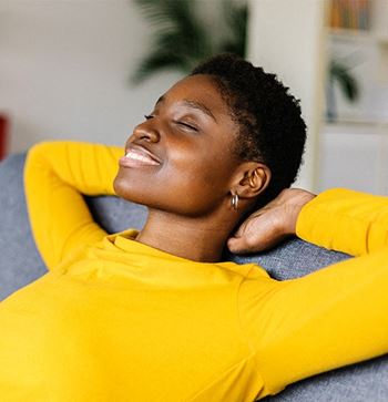 a woman in a yellow sweater smiles while sitting on a couch